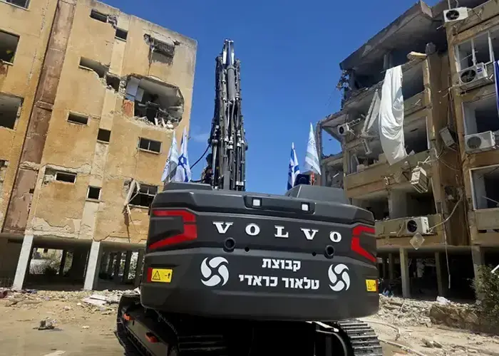 מחפר של הקבוצה מול בניין בהריסה